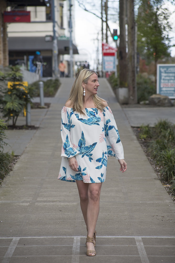 A woman walking down the sidewalk wearing a dress.