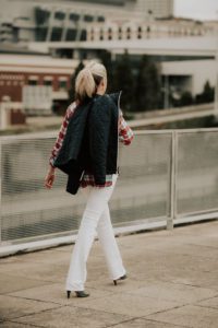 A woman walking down the street wearing white pants.