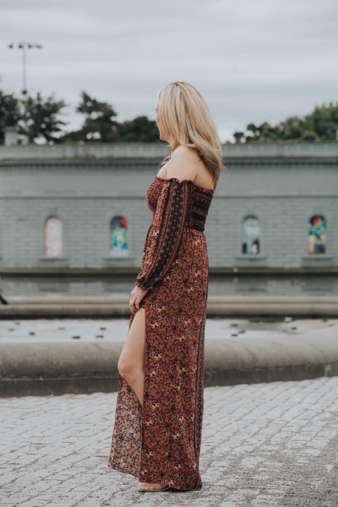 A woman in a long dress standing on the sidewalk.